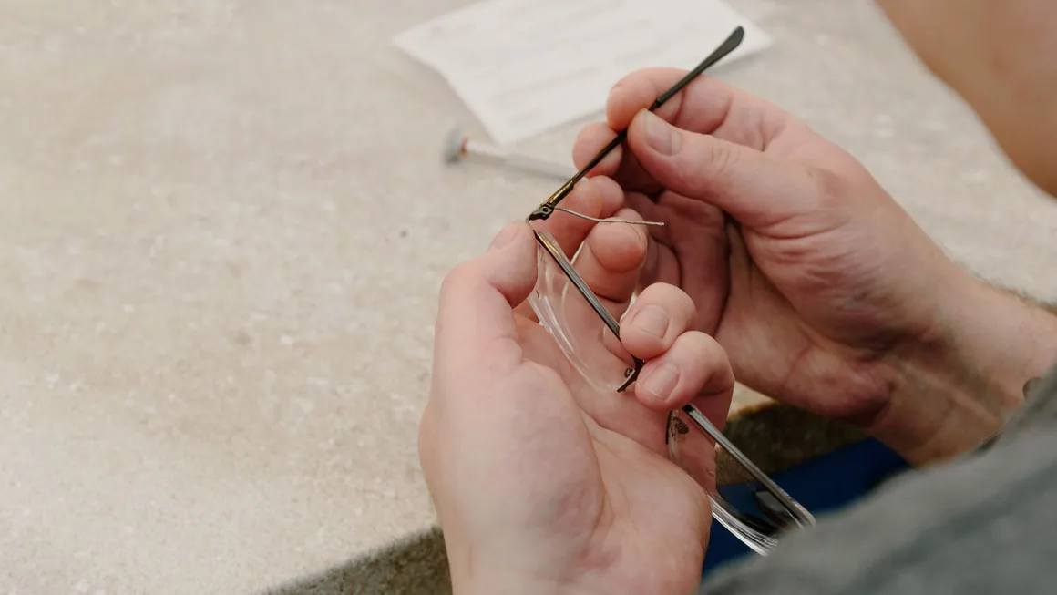 Manos sujetando una montura de gafas y colocando una varilla sobre el banco de un taller